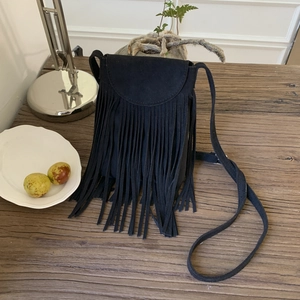 Close-up of black fringe crossbody bag with long tassels on a rustic wooden table