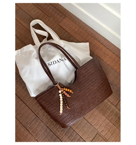 Detail view of dark brown woven tote bag with colorful beaded tassel charm and leather texture