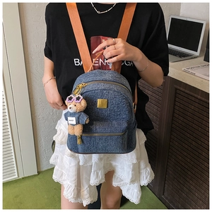 Dettaglio zaino in denim blu con logo in metallo dorato e ciondolo orsetto alla moda