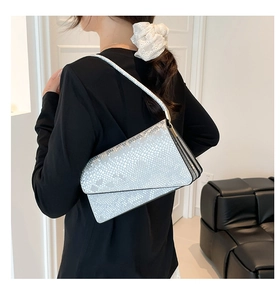 Detailed view of silver snakeskin shoulder bag worn by model in a modern room