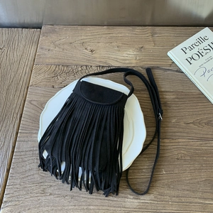 Detailed close-up of black fringe crossbody bag with suede texture on a wooden table