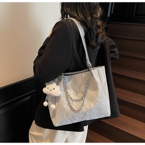 Detail of silver tote bag featuring pleated texture, metal chains, and a white plush charm