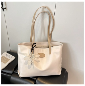 Detail of cream leather tote bag with logo patch and floral charm on leather seat
