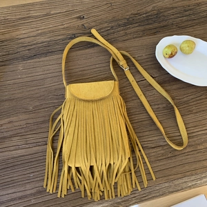 Flat lay view of a yellow suede crossbody phone bag with long tassels on wooden surface