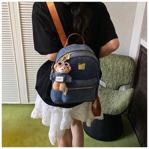 Dettaglio zaino in denim blu con spallacci marroni e ciondolo a forma di orsetto