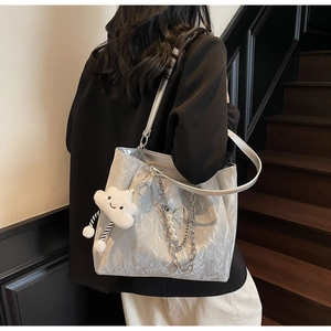 Detail view of silver pleated tote bag with chunky chains and pearl charms shown on model