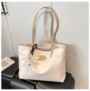 Detail of minimalist cream tote bag with floral charm and brown straps on a bench