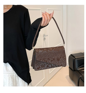 Detail of dark brown snakeskin texture and gold metal hardware on women shoulder bag