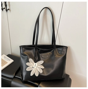 Detail of black leather tote bag with embossed logo and white 3D flower pendant charm