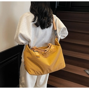 Detailed view of large mustard yellow nylon duffel bag with pleated texture and adjustable strap