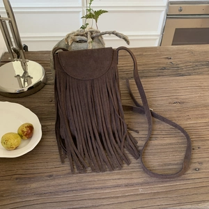 Detailed view of dark brown suede crossbody bag with long fringes on a wooden table