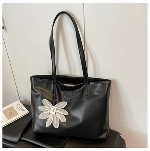 Close-up of minimalist black tote bag with smooth texture and a white floral charm