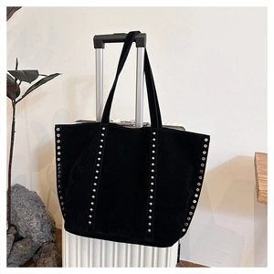 Close-up of black suede tote bag with silver rivets hanging on a white suitcase