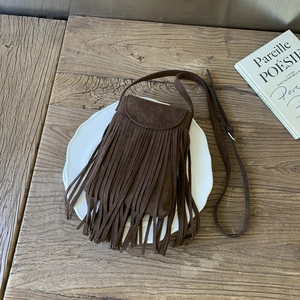 Flat lay of vintage dark brown suede crossbody bag with long tassels on ceramic plate