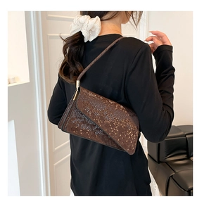 Detail of dark brown snakeskin embossed underarm bag with asymmetric flap shown on shoulder
