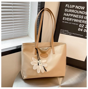 Detail of beige tote bag with long straps and white flower charm on a silver table