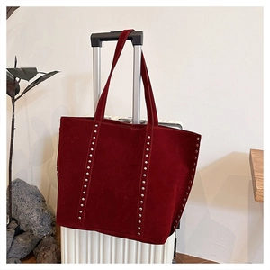Close-up of burgundy suede tote bag with silver studs hanging on a white suitcase