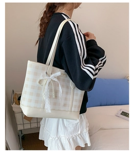 Detail of checkered tote bag with lace bow and pearl charm on a stylish model
