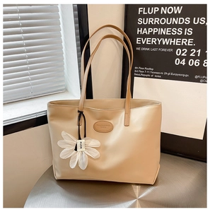 Detail of a beige PU leather tote bag with a white flower charm on a metal table