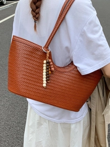 Brown woven leather tote bag with stylish beaded tassel shown on female model street shot