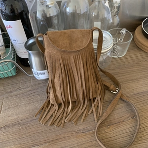 Close-up of brown suede crossbody bag featuring long fringes on a wooden surface