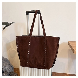 Detailed view of a brown suede tote bag with silver studs hanging on a white suitcase