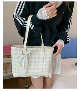 Detail of cream plaid tote bag featuring elegant lace and pearl bow charms on the front