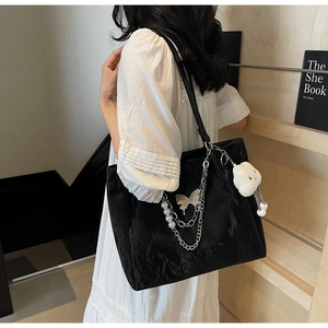 Detail of large black tote bag with silver chains, pearl charms, and plush doll pendant