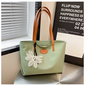 Detail of light green tote bag with orange handles and white floral charm in minimalist setting
