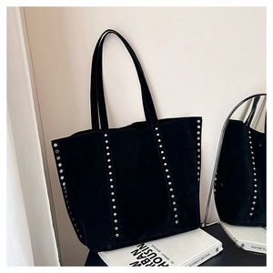 Detail of black suede tote bag with silver rivets placed against a minimalist wall