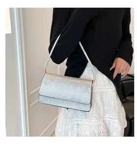 Detail shot of a silver snakeskin textured handbag worn with a chic black and white outfit