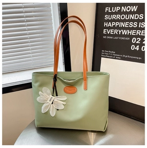 Detail of light green tote bag with brown straps, floral charm and logo patch on desk