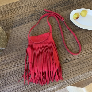 Detailed close-up of a red suede crossbody bag with long tassels on a rustic wooden table