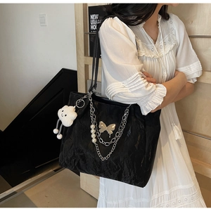 Detail of black tote bag with gold butterfly, chains, and white cloud plush charm
