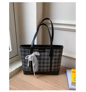 Detail of checkered tote bag featuring a leather strap and a lace bow charm accessory
