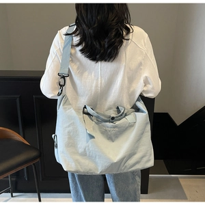 Rear view of model wearing a light blue large capacity travel duffel bag with wide strap