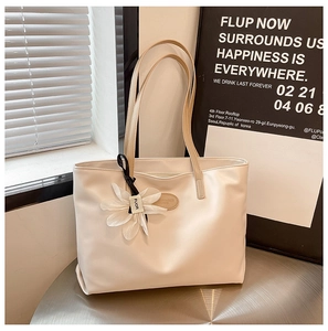 Detail of cream tote bag with floral charm and logo on a minimalist metal table