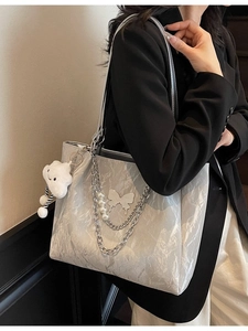 Silver metallic tote bag with chain strap and butterfly charm worn by a model