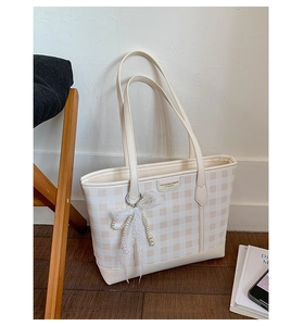 Close-up of cream checkerboard tote bag featuring a delicate lace bow and pearl pendant