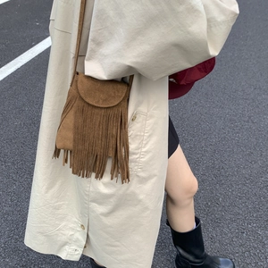Detailed view of bohemian brown suede crossbody bag with fringe tassels on a trench coat