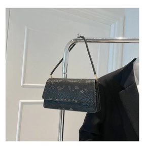 Detail of black snakeskin texture handbag on a silver rack with a black blazer backdrop