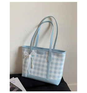 Close-up of blue plaid tote bag featuring pearl lace bow and decorative metal logo plaque