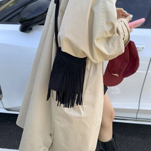 Close-up of small black suede crossbody bag with long tassel fringe and thin strap