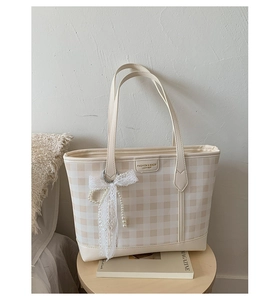Detail view of checkered tote bag with lace pearl bow charm on a wooden stool
