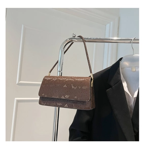 Detail of dark brown snake skin texture and gold hardware on a slim shoulder bag