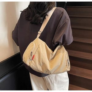 Detail of a large beige crossbody bag with red ribbon accent and multi-zipper pockets