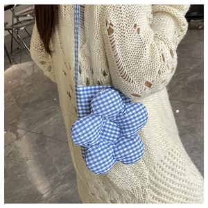 Détail d'un sac bandoulière à carreaux bleus avec une grande fleur porté par un mannequin