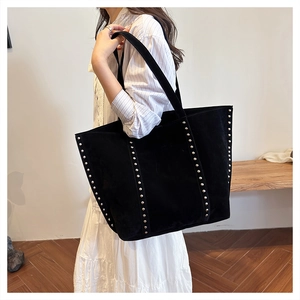 Detail of a large black tote bag with silver metal rivets and matte suede texture