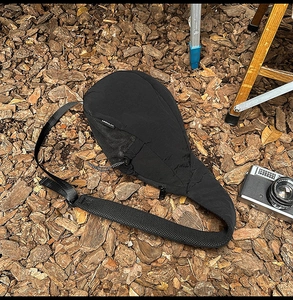 Close-up of black crossbody bag with adjustable strap on outdoor ground with camera gear