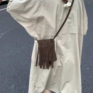 Detail of dark brown matte crossbody bag featuring bohemian long fringe tassels on model